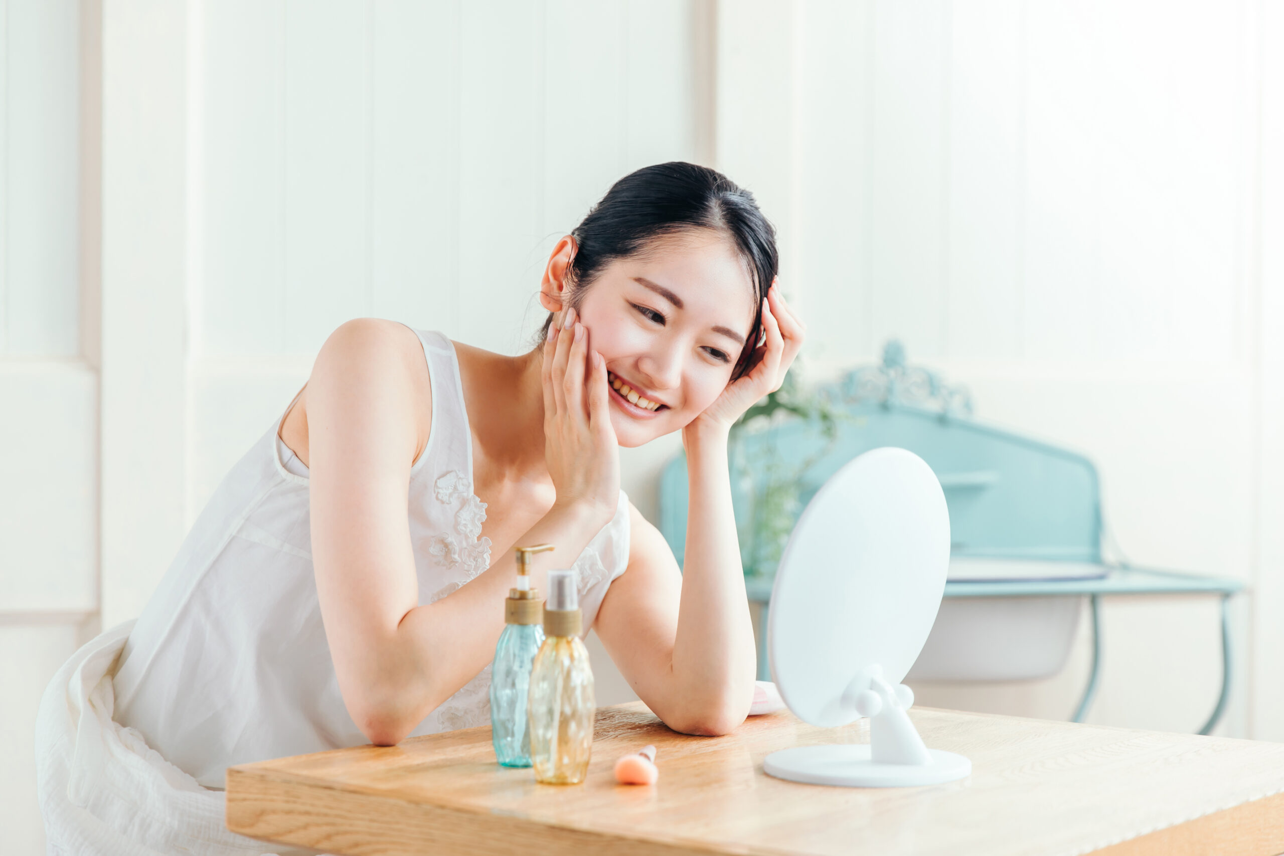 鏡を見ながら笑顔で肌に触れる女性